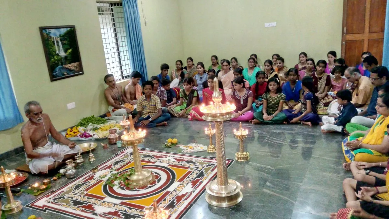 Ganapathi Homam and Bhagavathi Seva Pooja under way at Narayaneeyam, the priest at the kolam with children and families seated around three sides of the hall.