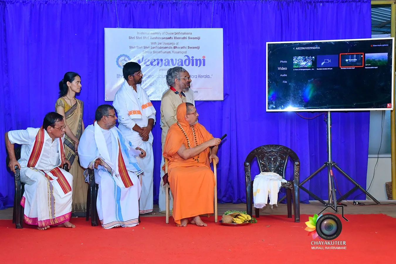 The video song release on stage: the Edneer swamiji in ochre robes seated with trustees and artistes beside a screen showing the ‘Sundara Kerala’ video.