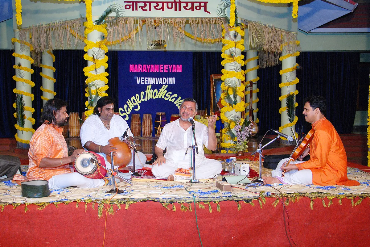 A Carnatic ensemble on the garlanded Narayaneeyam stage in 2013 — the vocalist at the centre with mridangam, tambura and violin — beneath the Sangeethothsavam banner.